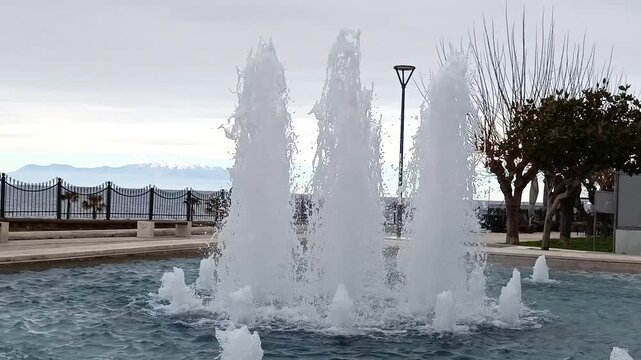 Beautiful water fountain spraying high in a public park by the sea on an overcast day, eb01