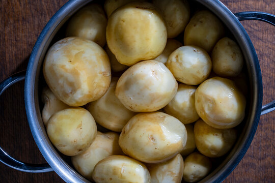 Peeled raw baby potatoes in a metal pot, top view. Closeup of fresh peeled young potatoes inside a stainless steel saucepan with water on a wooden table background