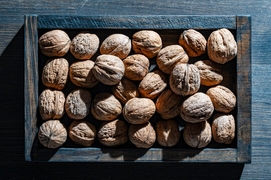 Whole walnuts in a rustic wooden tray top view. Closeup background of whole walnuts in a dark wooden box with dramatic side lighting and textures
