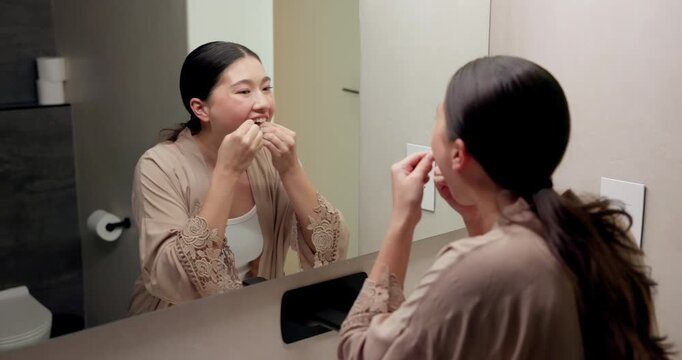 Mirror, home and asian woman with dental floss for oral hygiene or gum care in bathroom. Female person, string or morning routine with reflection or cavity for bacteria or germ removal in house