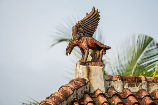 Terracotta eagle statue roof ornament on a clay tiled roof against clear sky.