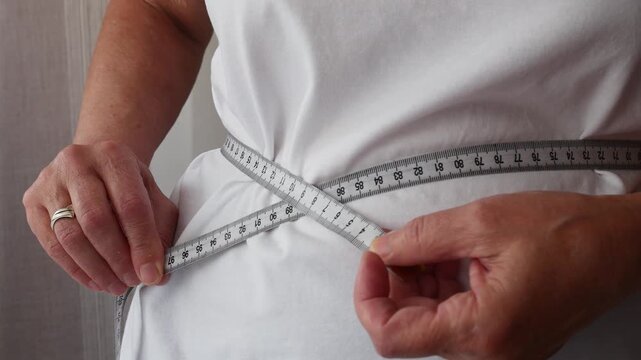 Senior woman tracking waist measurement with tape measure, weight management and healthy aging concept.