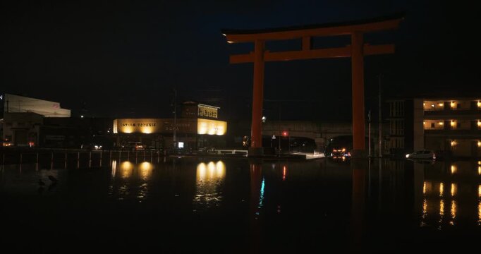 Massive torii gate over still, artificial pond at night - steady cam movement