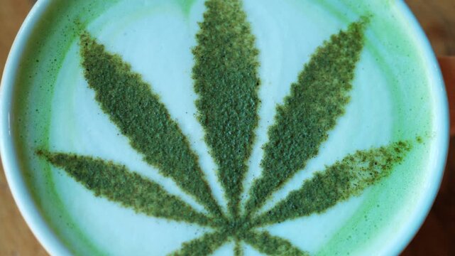 Top view of a matcha latte in a ceramic cup, decorated with powdered green tea forming a leaf pattern resembling a cannabis leaf