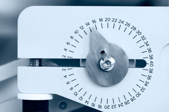 Close-up of white mechanical dial. Numbered scale ranges from 0 to 40. Metallic pointer moves along markings. Cylindrical rod connects via screw. Iindustrial measurement tasks