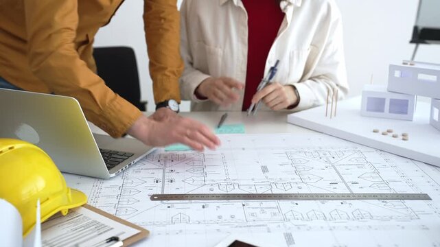 Engineering team collaborating on architectural blueprints, reviewing construction plans, and discussing building design concepts with tools and safety hard hat on table