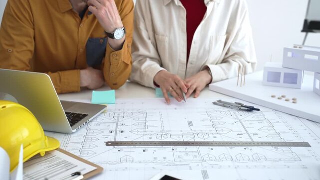 Engineering team collaborating on architectural blueprints, reviewing construction plans, and discussing building design concepts with tools and safety hard hat on table