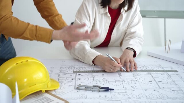 Engineering team collaborating on architectural blueprints, reviewing construction plans, and discussing building design concepts with tools and safety hard hat on table