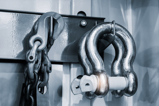 Close-up of industrial metal hardware, including chain and shackle. shackle features white pin and visible wear. Polished metal surfaces have brushed texture