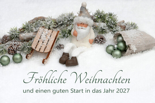Dekoration mit einem sitzenden Weihnachtsmann, einem kleinen Schlitten, Tannenzweigen, Zapfen und gr&uuml;nen Kugeln im Schnee mit dem Text 'Fr&ouml;hliche Weihnachten und einen guten Start in das Jahr 2027.