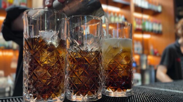 Cut crystal glasses filled with amber whiskey and ice cubes on a bar counter. Alcohol drink and nightlife concept.
