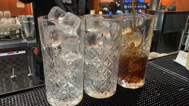 Cut crystal glasses filled with amber whiskey and ice cubes on a bar counter. Alcohol drink and nightlife concept.