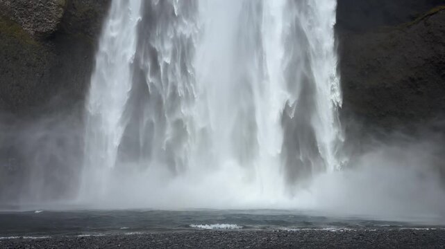 Powerful water plunging over the edge of Skogafoss waterfall in South Iceland, creating dense mist and dramatic movement against the rugged cliff face. This close-up nature video 