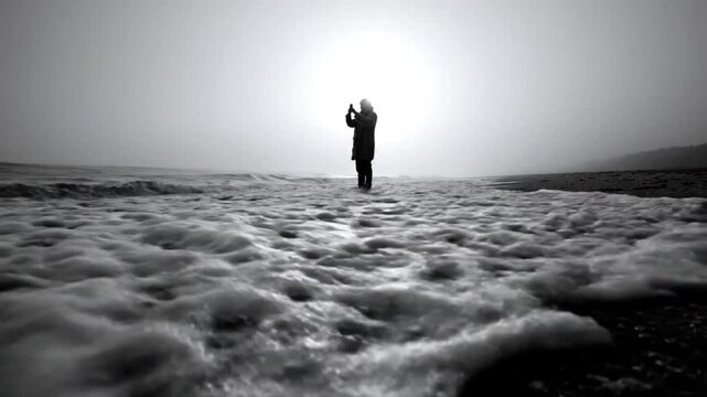 Lone Figure Capturing Ocean Waves on a Misty Beach Silhouetted by the Bright Sun in Monochrome