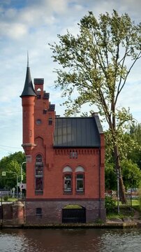 Distinctive red brick historic building with a narrow pointed tower rising beside trees under a clear sky. Kaliningrad
