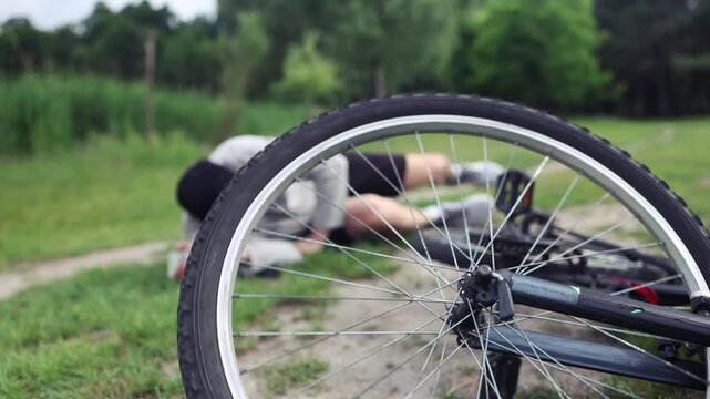 A young Caucasian man sits in a park after falling from a bike, calms the pain in his knee, is a dangerous bike ride in the park on an summer day