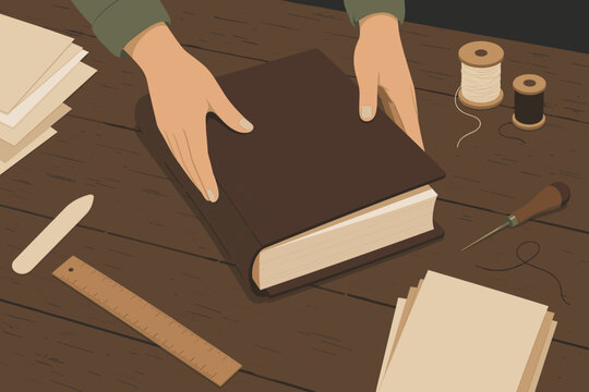 Hands holding a leather bound book cover on a wooden workbench with professional bookbinding tools like thread spools, an awl, a ruler, and paper for traditional handmade craft