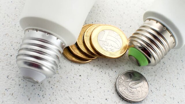 Bright light bulb on Brazilian coins, illustrating the concept of economy and its implications on the electricity bill.