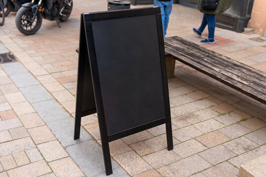 Empty black A frame sidewalk sign placed in a pedestrian zone, ideal for restaurant menus, cafe promotions