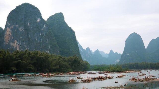 Picturesque landscape of China li river featuring numerous traditional bamboo rafts carrying tourists through stunning karst mountain scenery of guilin on an overcast day. Summer holidays