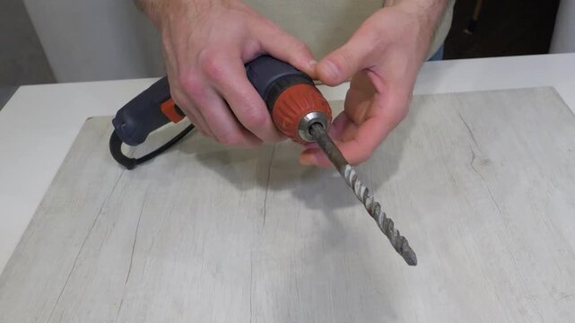 Clamping a drill bit into a drill with a man's hands. An electric drill with a drill bit inserted into the drill