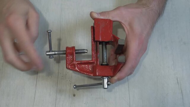 A person holding a mini sliding vise. Unscrewing the clamp on the vise.