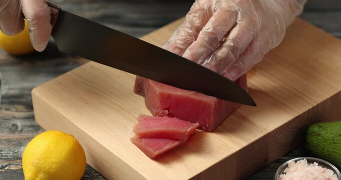 Gloved cook's hand cuts raw tuna steak into slices