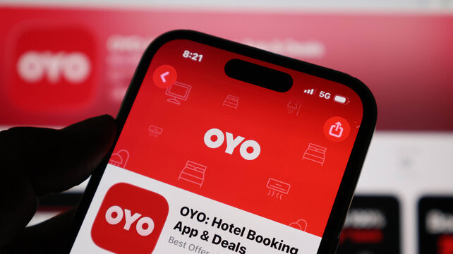 Closeup of a smartphone screen displaying the oyo hotel booking app interface, held in a hand against a blurred background