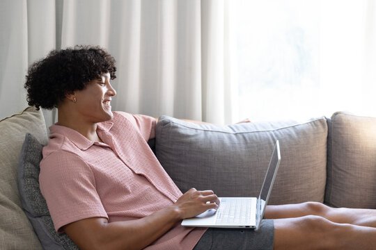 Laptop is resting on light-gray couch with cushions near bright window, soft light filtering