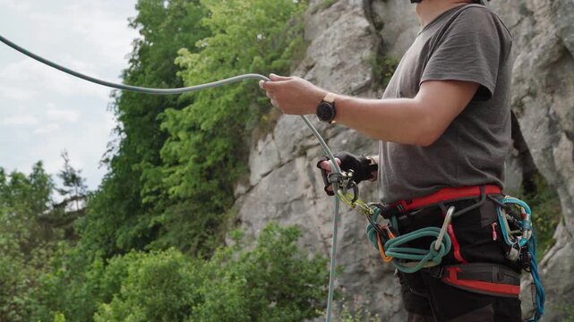 4K close up of a climber belaying his partner with a belay device on a harness at an outdoor cliff site. Rock climbing safety gear, rope management, and extreme sport concept