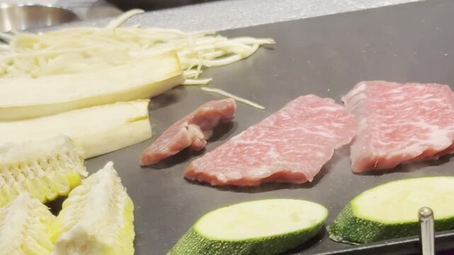 Premium marbled beef strips searing on a teppanyaki grill alongside fresh enoki mushrooms, corn, zucchini, and eggplant. Perfect for gourmet dining, asian barbecue, and culinary concepts.