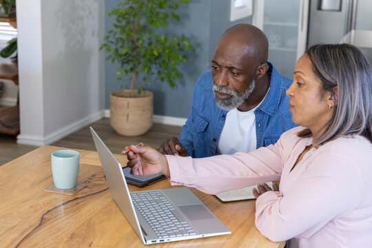 Senior couple reviewing household finances at kitchen table with pen, open notebook, laptop