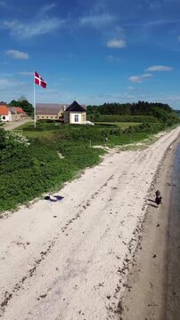 Aerial drone video tracking along a sandy beach towards the historic yellow tea house in denmark with the Danish flag waving proudly