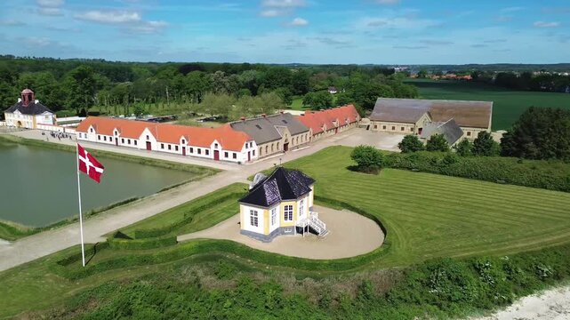 Beautiful aerial drone video of the historic yellow tea house pavilion and large estate buildings at Valdemars Slot on Tasinge island with a waving Danish flag