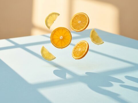 Fresh orange and lemon slices suspended in midair on a light blue table
