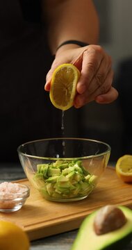 Cook's hand squeezes lemon juice into avocado pieces in bowl. Vertical video