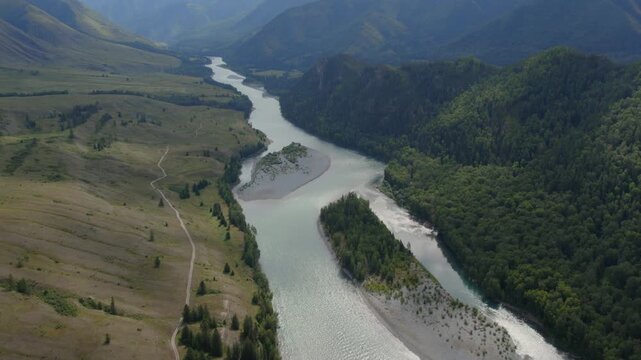 Drone footage of a winding river with sandbars flowing through the Ak-Kem Valley, Altai Mountains, Russia, with forested slopes and open meadows in summer