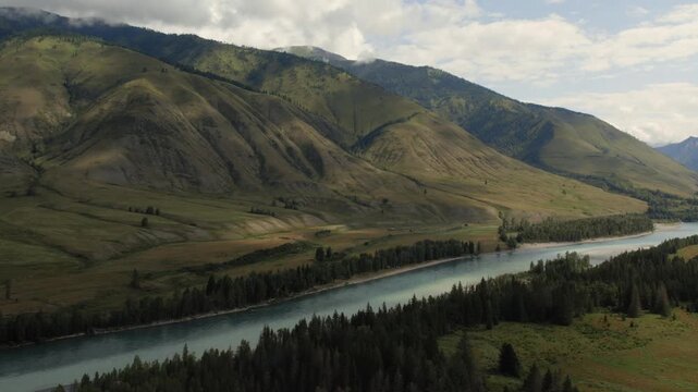 Wide cinematic view of the Ak-Kem valley with turquoise river, forest and rolling mountain slopes under cloudy sky, Altai Republic, Russia, remote wilderness scenery