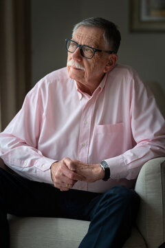 Thoughtful senior man with hearing aid sitting indoors and looking away