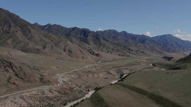 Drone footage of the Chuysky Trakt road crossing a wide mountain valley with river and dry steppe hills near Inya, Altai Republic, Russia on a clear day