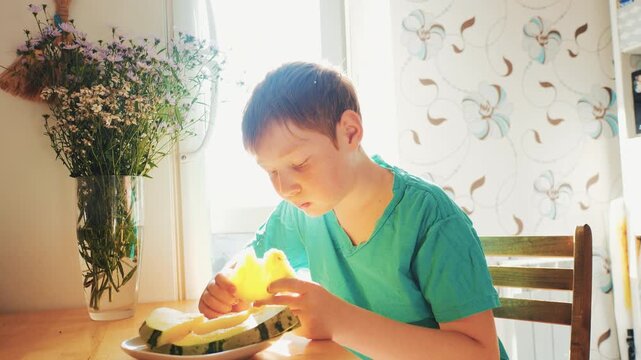 Cute boy happily eating a slice of melon for breakfast