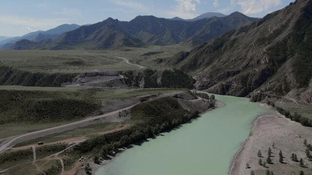 Drone footage of Chuysky Trakt winding through a wide mountain valley with turquoise river, rocky slopes and green hills, Altai Republic, Russia in summer daylight