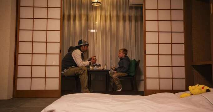 Father and son eating at a small table in Japanese themed room - wide shot