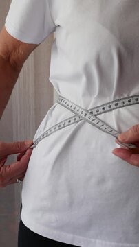 Senior woman tracking weight loss progress by measuring waist with tape measure.