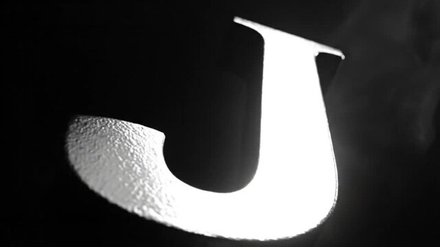 Dramatic monochromatic letter J illuminated by bright light against dark background with visual texture