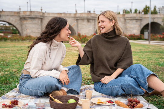 Two women sharing picnic snack and laughter in a park