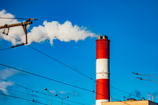 A red and white chimney with white smoke against a blue sky