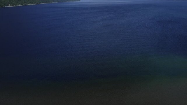 Drone footage of Lake Teletskoye with calm deep blue water and forested mountain slopes under a clear sky, Altai Republic, Russia, scenic wilderness landscape