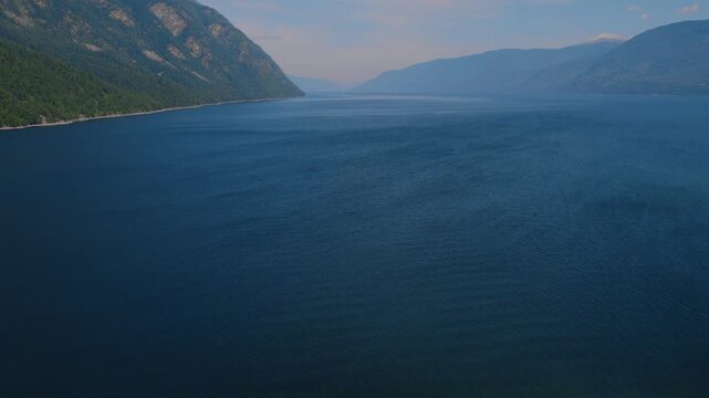 Wide aerial footage of Lake Teletskoye surrounded by forested mountains and cliffs on a clear summer day, Altai Republic, Russia, tranquil nature landscape