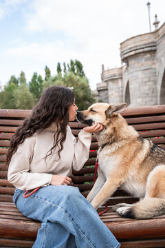 Woman kissing her dog on bench in city park outdoors